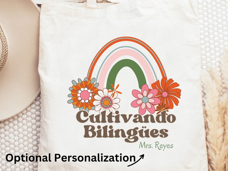 Op de afbeelding: Een witte tote bag met een regenboog, bloemen en de tekst "Cultivando Bil&iacute;ng&uuml;es" in bruine letters. De tekst "Mrs. Reyes" staat in kleinere bruine letters onder de hoofdtekst.