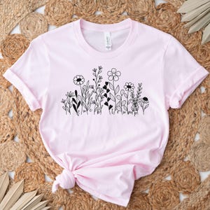 May include: A pink t-shirt with a black floral design and the text "Believe" and "Triumph" printed on the front.