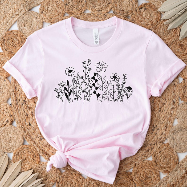 May include: A pink t-shirt with a black floral design and the text "Believe" and "Triumph" printed on the front.