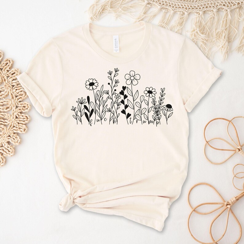 May include: A cream-colored t-shirt with a black floral design and the text "We are all just a little bit wild".