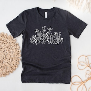 May include: A dark gray t-shirt with a white graphic of a field of flowers. The flowers are simple line drawings with the words "luck" and "happy" written in the stems.