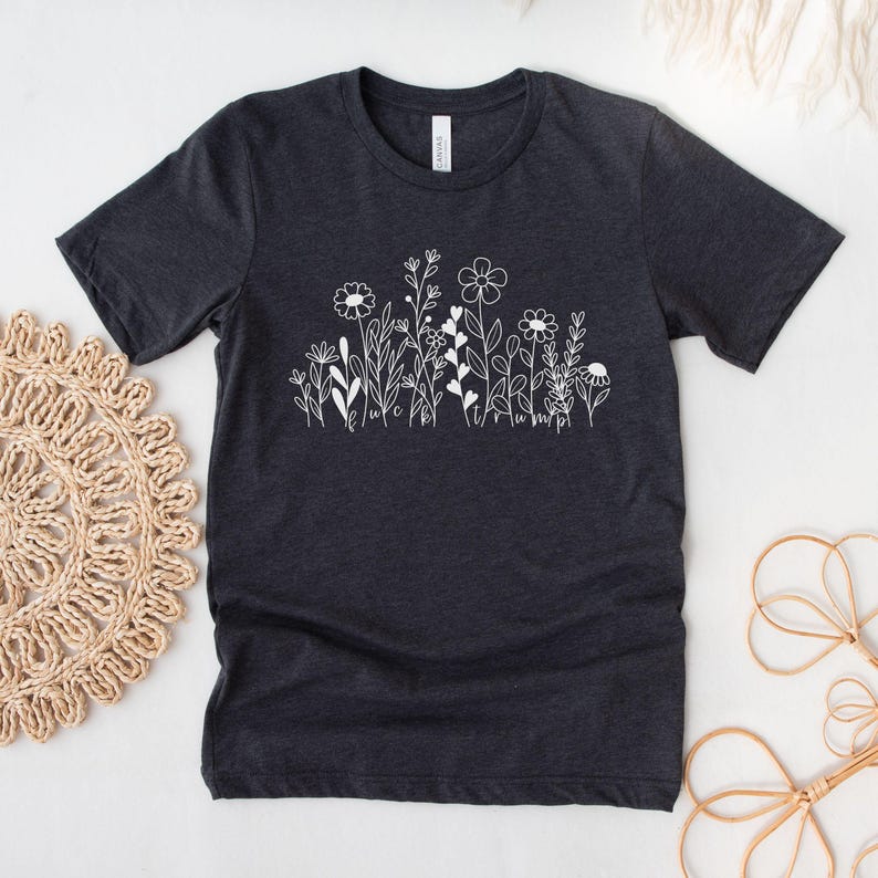 May include: A dark gray t-shirt with a white graphic of a field of flowers. The flowers are simple line drawings with the words "luck" and "happy" written in the stems.