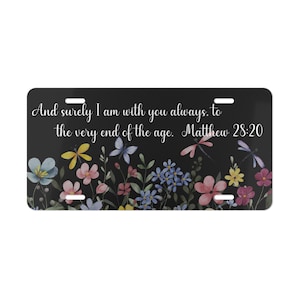 以下が含まれることがあります： 黒いナンバープレート。花柄のデザインと「And surely I am with you always, to the very end of the age. Matthew 28:20」のテキスト。花はピンク、黄色、青、紫の色合いです。