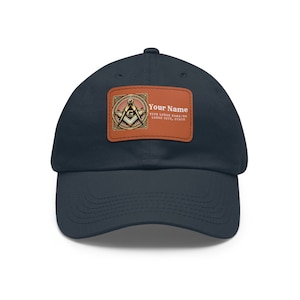 Op de afbeelding: Een marineblauwe baseballpet met een bruine leren patch met een gouden vrijmetselaarsymbool en de tekst "Your Name", "Your Lodge Name/No", "Lodge City, State".