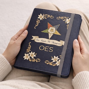 May include: A dark blue notebook with a gray elastic closure band. The cover features a gold five-pointed star emblem, floral corner accents, and a banner with the text Sis Renie M. Thompson above the letters OES printed in gold lettering.