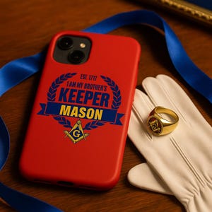 May include: A red phone case with the text "I AM MY BROTHER'S KEEPER MASON" and a Masonic symbol. A gold ring with a Masonic emblem rests on a white glove. A blue ribbon is in the background.