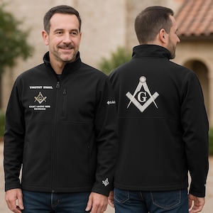 May include: Black zip-up jacket with embroidered Masonic symbols and text. The jacket features a stand-up collar, front pockets, and the name "Timothy Shaul" above the Masonic emblem. The back of the jacket displays a larger Masonic symbol.