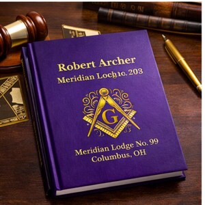 Könnte beinhalten: Ein lila Buch mit goldener Schrift und einem Freimaurer-Emblem. Auf dem Einband steht "Robert Archer Meridian Loch 10. 203" und "Meridian Lodge No. 99 Columbus, OH". Ein Hammer und ein Stift sind sichtbar.