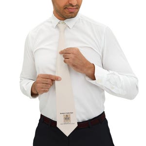 May include: A white tie with a beige background featuring a Masonic symbol and the text "Brother's Name Here" in a brown font.