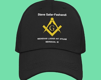 May include: Black baseball cap with white text that reads "Steve Safar-Fashandi", a yellow and gold Masonic symbol with a "G" in the center, and the text "MERIDIAN LODGE #47 AF&AM MERIDIAN, ID"