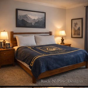 Può includere: Una camera da letto con un letto in legno e una coperta blu navy con un bordo dorato e un disegno centrale. Due cuscini bianchi sono sul letto. Un dipinto di paesaggio è appeso sopra il letto.