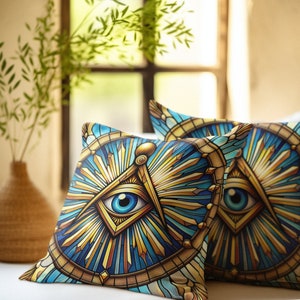 May include: Two decorative throw pillows with a stained glass design featuring an all-seeing eye and a compass and square. The pillows are on a white bed with a wooden headboard and a window in the background.