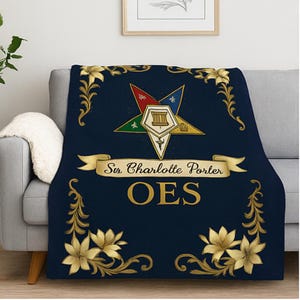 May include: Navy blue throw blanket with gold floral accents and a central emblem. The emblem features a star with various colored points and a banner that reads "Sir Charlotte Porter OES".