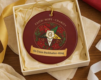 May include: A burgundy round ornament with gold trim and a gold hanging cord, presented in a white box. The ornament features the words "FAITH HOPE CHARITY" and a star design with the text "Sis Gwen Buckhalter-King".