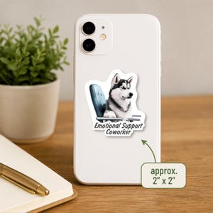 Pu&ograve; includere: Uno smartphone bianco con un adesivo raffigurante un cane husky bianco e nero seduto su una sedia da ufficio blu. L'adesivo include il testo Emotional Support Coworker e misura circa 5 cm per 5 cm.
