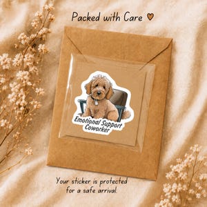 May include: A square sticker featuring a brown doodle dog sitting in an office chair with the text Emotional Support Coworker, enclosed in a clear plastic sleeve on a brown paper envelope with the printed text Packed with Care.
