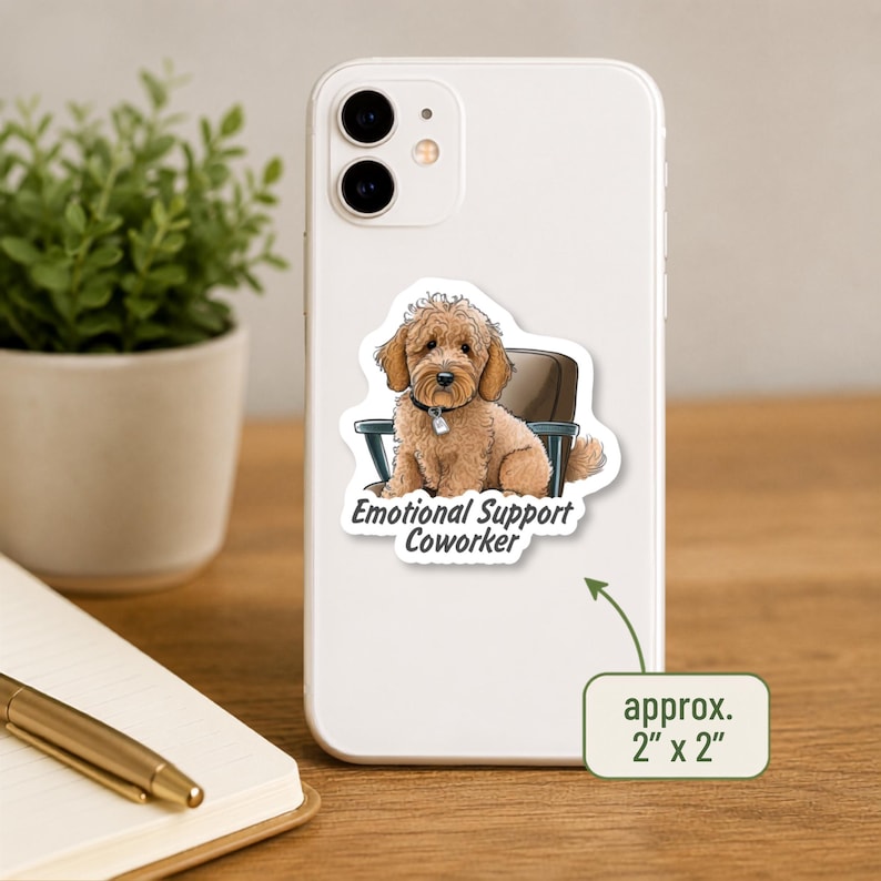 May include: A white smartphone featuring a sticker of a light brown curly-haired dog sitting in a dark chair. The text below the dog reads Emotional Support Coworker. A green arrow points to a box stating the sticker is approximately 2 inches by 2 inches.