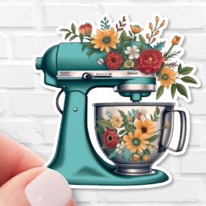 May include: A teal stand mixer with a floral design on the bowl. The mixer has a silver handle and a silver knob on the side. The bowl is filled with colorful flowers.