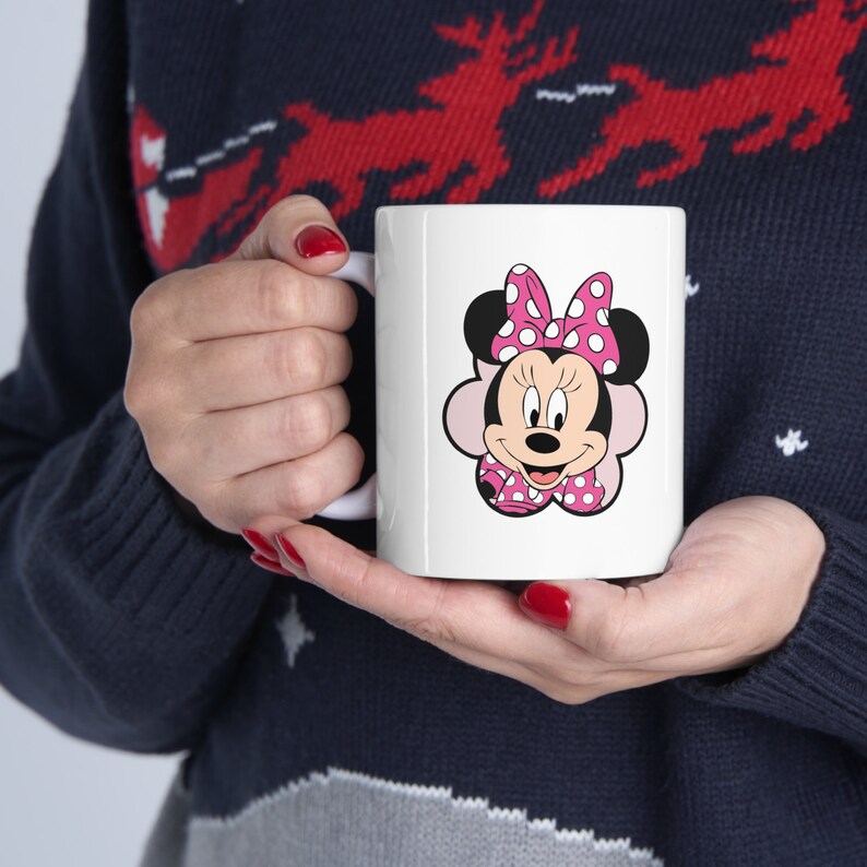 May include: White ceramic mug with a colorful cartoon image of Minnie Mouse wearing a pink bow with white polka dots.