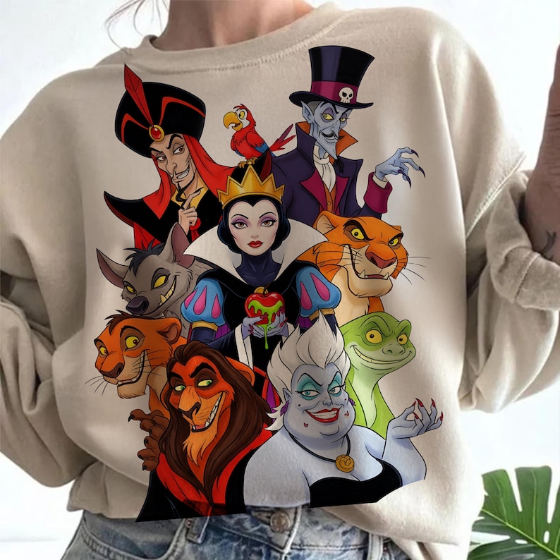 Puede incluir: Sudadera beige con un gr&aacute;fico colorido de villanos animados. El dise&ntilde;o incluye personajes como Jafar, la Reina Malvada, &Uacute;rsula y Scar. La obra de arte est&aacute; detallada con colores vibrantes e ilustraciones de estilo caricatura.