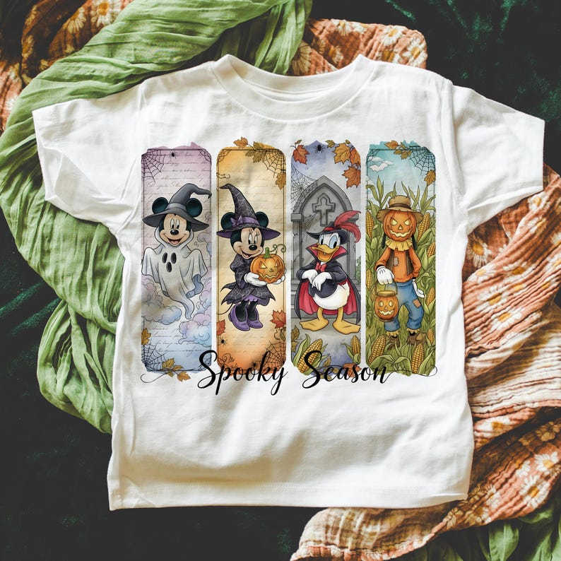 May include: White t-shirt featuring a Halloween-themed design with Mickey Mouse as a ghost, Minnie Mouse with a pumpkin, Donald Duck in a cape, and a scarecrow. The words "Spooky Season" are written in a script font.