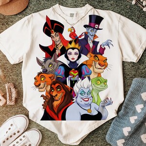 Puede incluir: Camiseta blanca con un gr&aacute;fico colorido de villanos de Disney, incluyendo Jafar, la Reina Malvada y &Uacute;rsula. El dise&ntilde;o presenta ilustraciones detalladas de los personajes, con colores vibrantes y contornos audaces. La camiseta es de material suave.