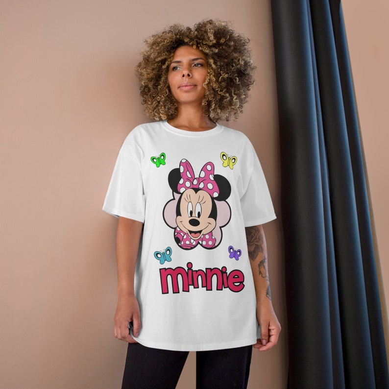May include: White t-shirt with a colorful graphic of Minnie Mouse wearing a pink bow and a polka dot dress. The shirt also has the word "Minnie" printed in red letters.