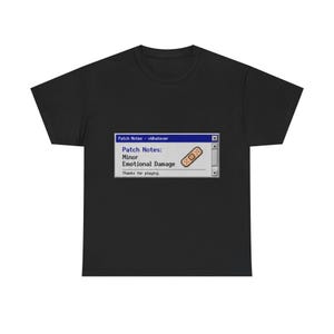 May include: A black short-sleeved t-shirt featuring a graphic of a computer dialog box titled Patch Notes - vWhatever. The text reads Patch Notes: Minor Emotional Damage, Thanks for playing, accompanied by a small pixelated adhesive bandage icon.
