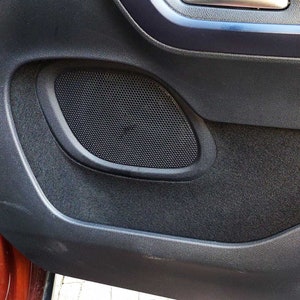 May include: A close-up of a black car door panel with a speaker grille. The speaker grille is oval-shaped and has a black plastic frame.