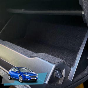 Op de afbeelding: Een blauwe Ford Focus auto is te zien in de linkerbenedenhoek van de afbeelding. De rest van de afbeelding toont de binnenkant van het dashboardkastje van een auto, dat is bekleed met zwart tapijt.