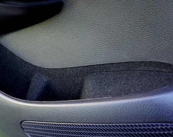 May include: A close-up of the interior of a car door, showing a black fabric storage compartment and a black speaker grille.