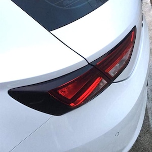 Può includere: Primo piano della parte posteriore di un'auto bianca, che mostra un elegante fanale posteriore. Il fanale posteriore presenta una luce rossa racchiusa in un alloggiamento scuro e oscurato, in contrasto con la carrozzeria bianca. Il design è moderno e aerodinamico.