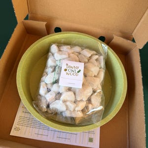 May include: A cardboard box with a green bowl inside, holding a clear bag of small, white stones. The bag is labelled "TAWNY OWL WOOD". A leaflet is also present in the box. The bowl is approximately 20 cm in diameter.