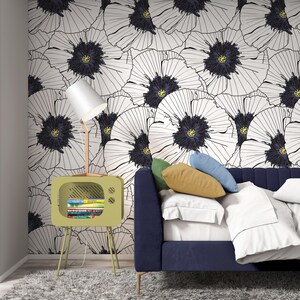 May include: A green TV-shaped side table with a shelf for books, a white lamp with a white shade, and a blue couch with white and yellow pillows in front of a white wall with a black and white floral pattern.