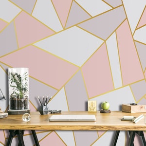 Puede incluir: Papel pintado geométrico con un patrón de formas rosas, grises y blancas, delineadas con líneas doradas. Un escritorio de madera con un terrario, lápices y un portátil frente al papel pintado.