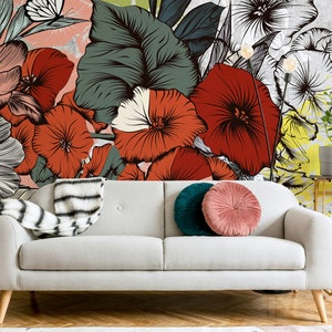 May include: A white sofa with two pillows, one green and one pink, in front of a wall with a large floral mural featuring red, white, and green flowers.