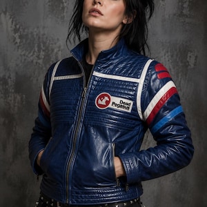 May include: A blue leather jacket featuring a stand-up collar, a front zipper, and quilted shoulder panels. The chest displays a circular patch with a white pegasus icon and the text Dead Pegasus. Red, white, and blue stripes accent the sleeves.