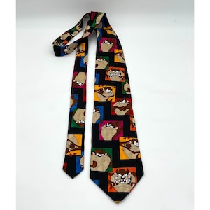 May include: A black necktie featuring a repeating pattern of the Tasmanian Devil cartoon character in colorful squares. The tie has a classic design with a pointed end and is made of a smooth fabric.