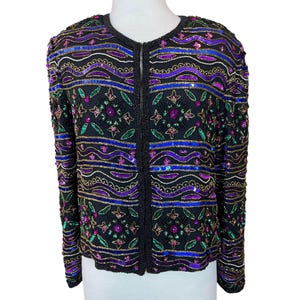 Könnte beinhalten: Schwarze Jacke mit Perlenbesatz, rundem Ausschnitt und langen Ärmeln. Die Jacke ist mit Pailletten und Perlen in Lila, Blau, Grün und Gold verziert. Die Jacke hat einen Reißverschluss.