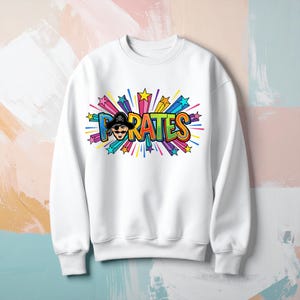 May include: White sweatshirt featuring the word "PIRATES" in a colourful, cartoon-style graphic. The design includes a pirate wearing a black hat, surrounded by starbursts in various colours like blue, green, yellow, and pink.