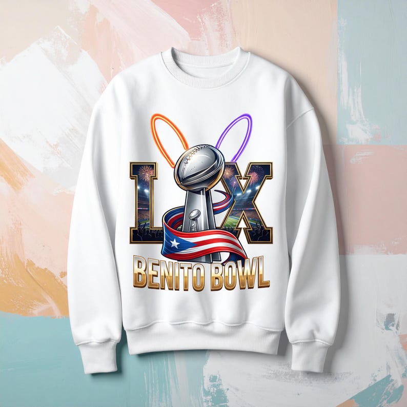 Pode incluir: Camisola branca com um gr&aacute;fico de um trof&eacute;u prateado, os algarismos romanos LX e o texto "BENITO BOWL". O design inclui uma fita com a bandeira de Porto Rico e arcos laranja e roxos.