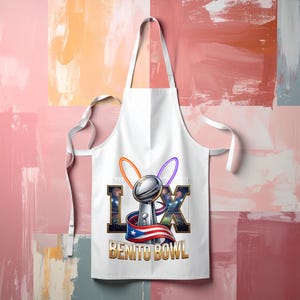 Pode incluir: Avental branco com um design de trof&eacute;u de futebol e o texto "LX BENITO BOWL". O design inclui a bandeira de Porto Rico, fogos de artif&iacute;cio e an&eacute;is laranja e roxos. O avental tem um bolso e la&ccedil;os brancos.