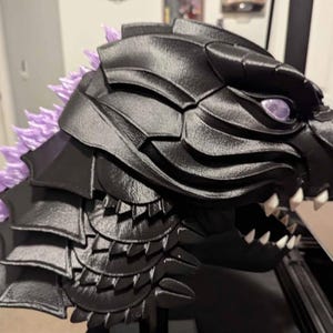 May include: A black and purple 3D printed monster head with sharp teeth and a textured surface. The head is on a black stand.