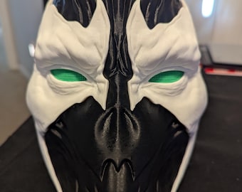 May include: A black and white 3D printed mask with green eyes. The mask has a detailed design with sharp edges and a textured surface.