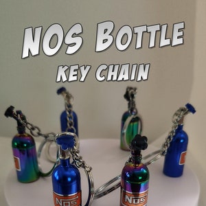 May include: Five NOS bottle keychains, two are iridescent blue and three are iridescent rainbow, with the NOS logo in orange. The keychains are on a white circular display stand with the text "2" in black.
