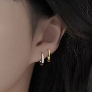 May include: A pair of small hoop earrings, one gold and one silver, worn in a person's earlobe.