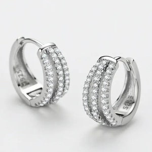 May include: Silver hoop earrings with a row of small cubic zirconia stones around the outer edge. The earrings are marked "925 S" on the back.