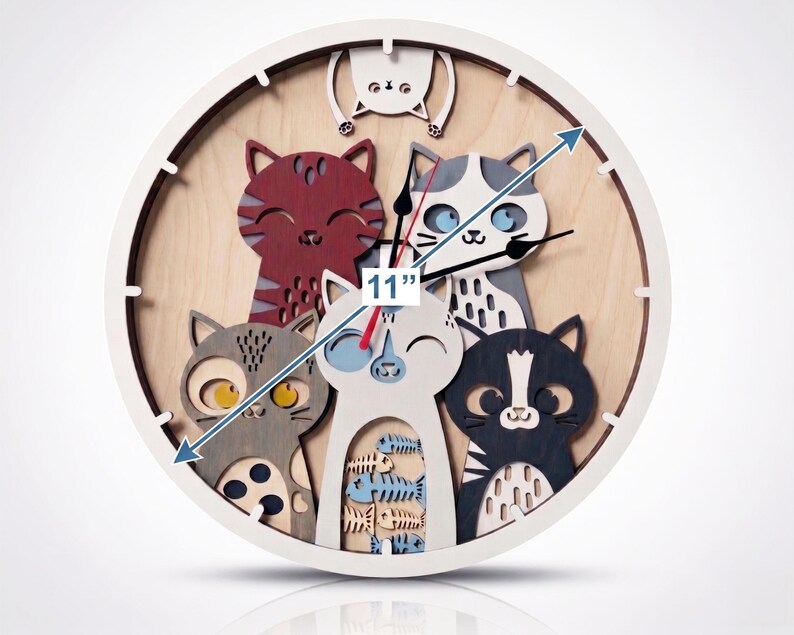 May include: A round, white-framed clock with a wooden face featuring a cat theme. The clock is 11 inches in diameter and has five cat figures in various colors. The clock hands are black.