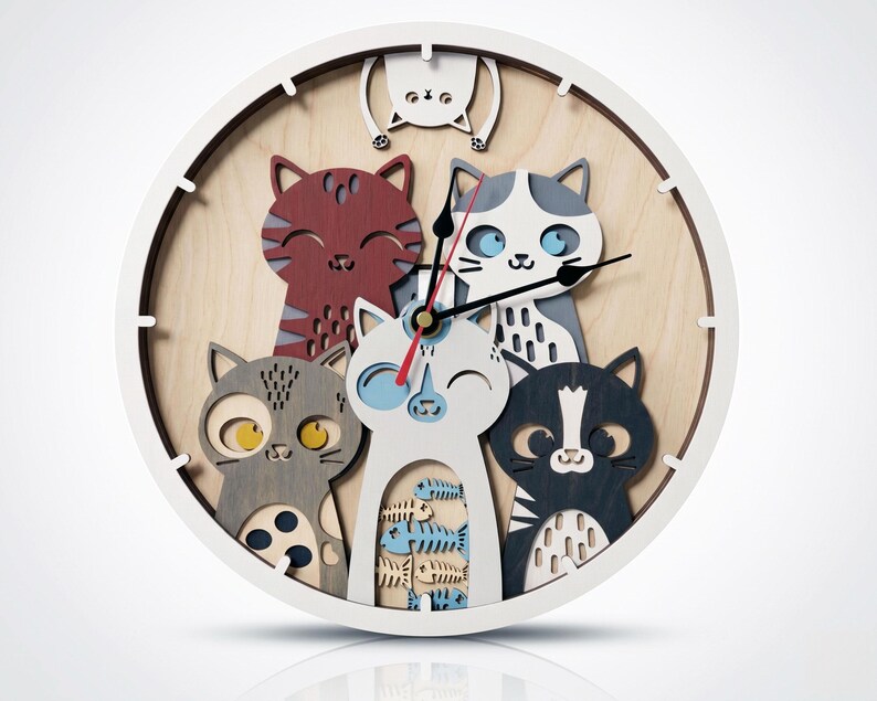 May include: A round wall clock featuring a playful design of five cartoon cats in various colors, including red, gray, and black. The clock has a white frame and a light wood-grain background, with black clock hands.