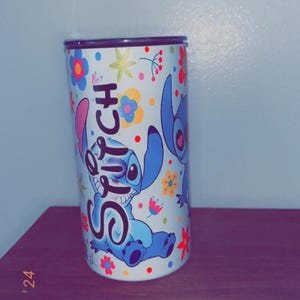 May include: A cylindrical tumbler featuring the character Stitch from the Disney movie Lilo & Stitch. The tumbler is white with a colorful floral pattern and the word "Stitch" in blue. The design includes images of Stitch.